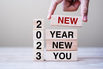 hand holding wooden block with text 2023 NEW YEAR NEW YOU on table background. Resolution,...