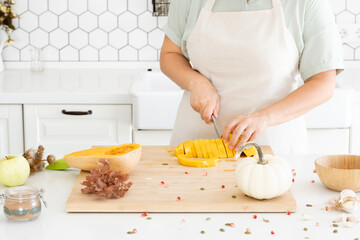 Woman hands slices a butternut pumpkin in modern white kitchen. Homemade autumn pumpkin soup recipe. Meal preparation