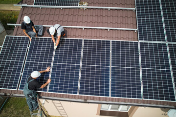 Men technicians mounting photovoltaic solar moduls on roof of house. Electricians in helmets...