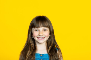 A cute little schoolgirl girl smiles broadly, her front milk teeth fell out in her mouth. The concept of a pediatric dentist and tooth loss. Empty space for signature.