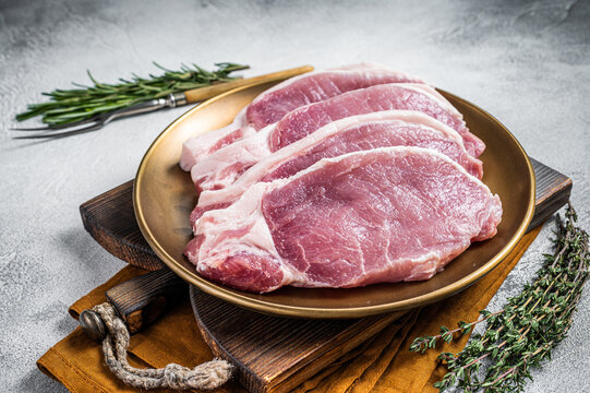 Fresh Raw Pork Cutlet Or Chop Steak On A Plate With Herbs. White Background. Top View