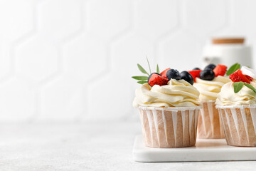 Vanilla cupcakes with fresh berries, buttercream, green leaves on grey background. Delicious...