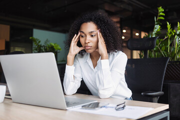 Stressed business woman sitting at office workplace looking at laptop computer. Tired and overworked businesswoman. Young exhausted student girl in stress.