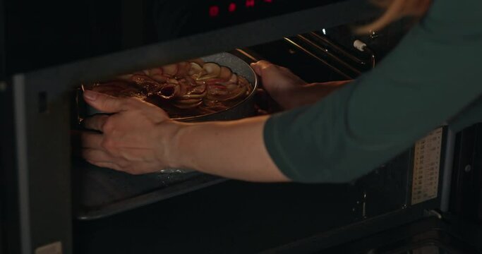 A woman puts an apple pie to bake in the oven. Medium shot. Slow-motion