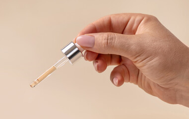 Female Hand holding pipette with drop falling down over light beige close up. Medical research