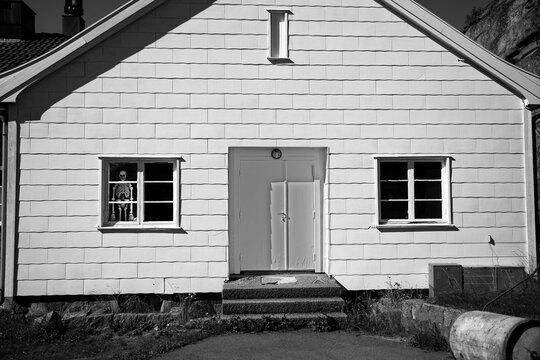 Abandoned, Haunted, White House With A Scary Skeleton Staring Out The Window From The Dark. Halloween Mode In This Black And White Image.