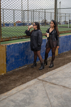 Vertical photo of two friends drinking a coffee in a football field