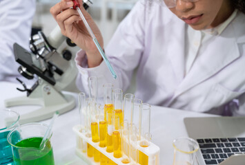 Young female scientist pipetting liquid into test tube next to microscope in science research...