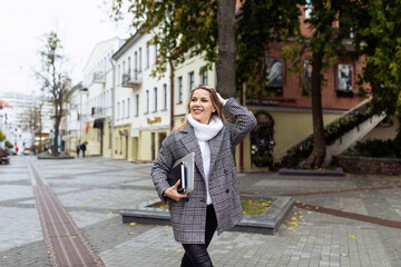 an adult woman lawyer with a smile on her face hurries to work with a laptop in her hands against the backdrop of a city panorama