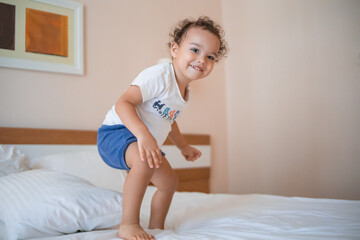 Curly toddler boy jumping and having fun on the bed