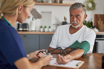 Caucasian female doctor measuring pressure of senior man at home visit