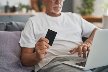 Close up of senior caucasian man sitting at couch and make shopping online