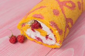 Obraz na płótnie Canvas Festive yellow biscuit roll with white cream and raspberries, concept, on pink wooden boards