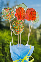 a lot of transparent lollipops, beautifully decorated, stand against the blue sky and greenery