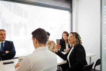 Smiling businesswoman photographing through smart phone in meeting at office