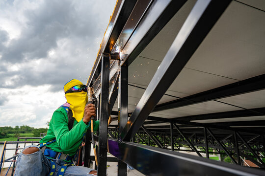 Picture of an Asian welder welding a steel structure in a factory building.