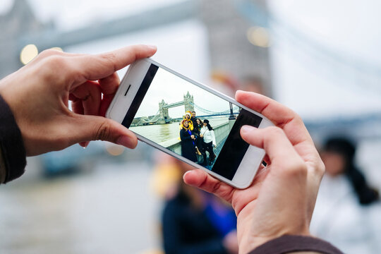 London, United Kingdom. A group of friends take pictures with a mobile phone in front of Tower Bridge