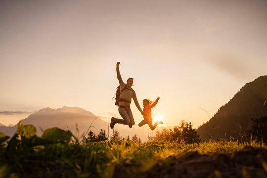 Happy man with daughter jumping on top of mountain