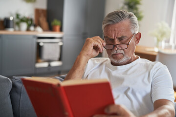 Senior caucasian man reading book and lying at the couch