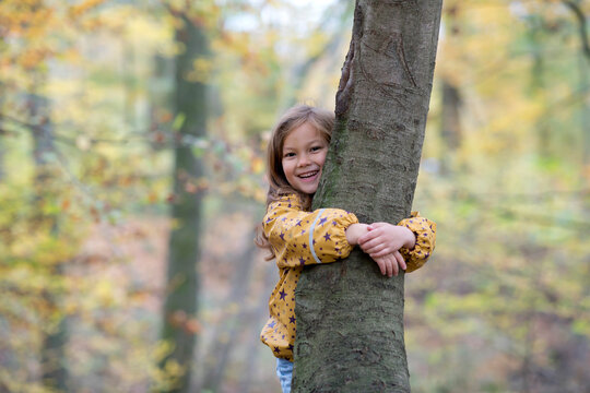 Happy cute girl hugging tree in forest - Powered by Adobe