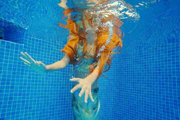 Redhead girl swimming underwater in pool