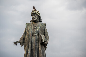An old statue, set against a grey, cloudy sky. The statue is located in Valencia, Spain