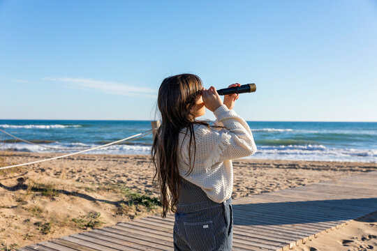 Girl watching sea through monocular on sunny day