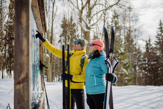 Senior couple looking at tourist board in the middle of snowy forest.