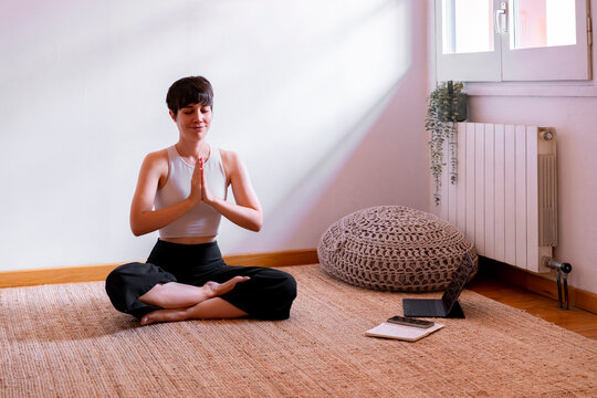 Woman sitting with eyes closed practicing yoga using tablet PC at home