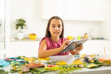 A child paints a picture of an autumn leaf with paints. Children's hands. Favorite hobby, materials for creativity.