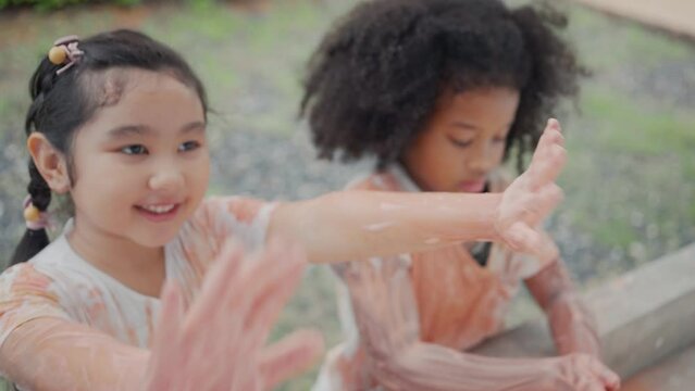 Group little asian and african american girls washing hands with soap on outdoor wash basin after painting color by using her hands. Kids hygiene and health concept.