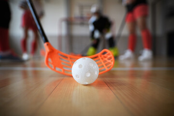Close-up of floorball stick and ball during woman floorball match in gym.
