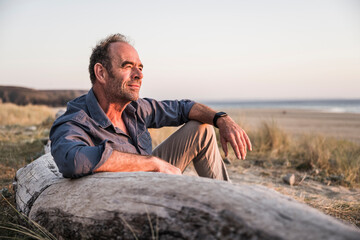 Mature man leaning on log enjoying sunset