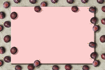 Pink surface with plums on a gray stone around the edge