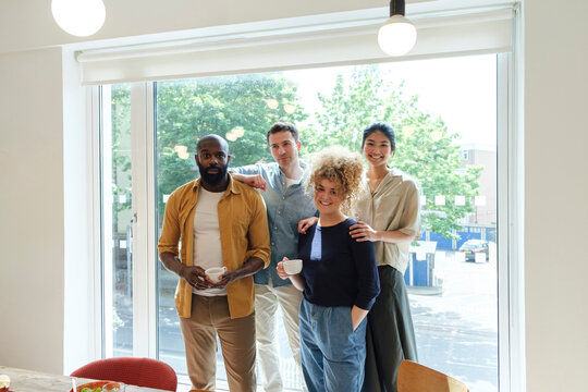 Smiling business people standing in front of window holding cups of coffee