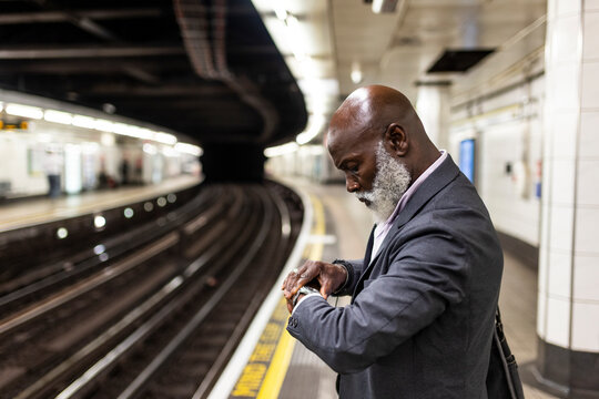 Senior businessman checking time on wristwatch waiting at subway station