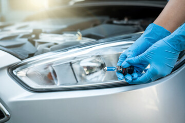 Close-up photo of a man's hands holding a car light bulb near the car for replacement.