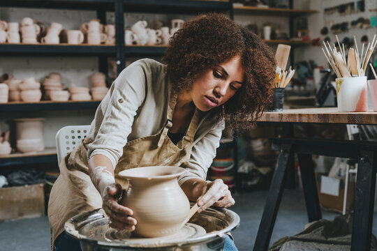 Young potter molding pot shape on pottery wheel at workshop