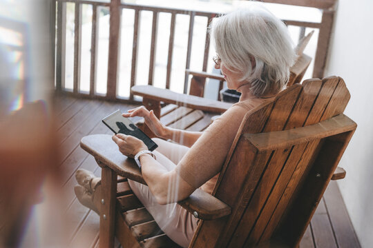 Mature woman sitting on chair using tablet PC at home terrace