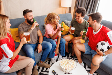 Football fans drinking beer and making a toast while watching world championship game on TV