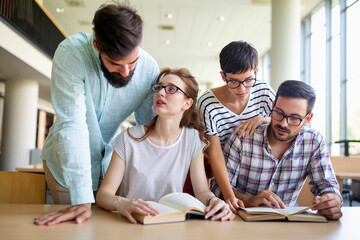 Fototapeta premium Happy university students studying with books in library. Group of multiracial people in college