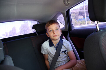 Fototapeta na wymiar The boy is wearing a seat belt sitting in the back seat of the car. Close-up portrait..