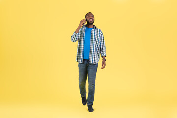 African Guy Talking On Phone Communicating Walking Over Yellow Background