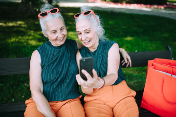 Senior women twins outdoors in city checking smartphone.