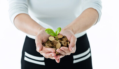 Businesswoman holding little tree  growing from pile of coins