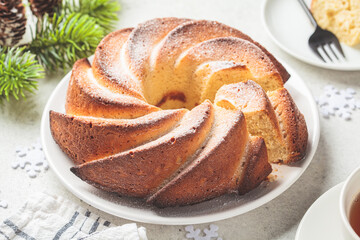 Christmas dessert. Vanilla pound cake with powdered sugar on white plate, light gray background with Christmas tree branches.
