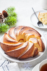 Christmas dessert. Vanilla pound cake with powdered sugar on white plate, light gray background with Christmas tree branches.