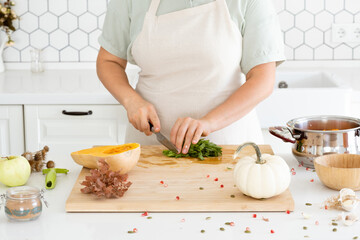 Obraz na płótnie Canvas Woman hands chopping parsley in modern white kitchen. Homemade autumn pumpkin soup recipe. Meal preparation.