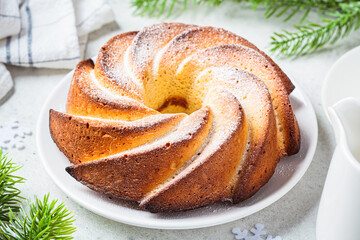 Christmas dessert. Vanilla pound cake with powdered sugar on white plate, light gray background with Christmas tree branches. - obrazy, fototapety, plakaty