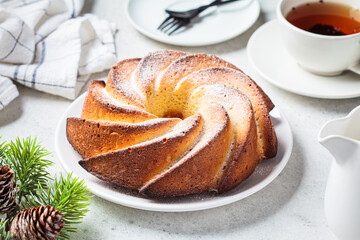 Obraz na płótnie Canvas Christmas dessert. Vanilla pound cake with powdered sugar on white plate, light gray background with Christmas tree branches.
